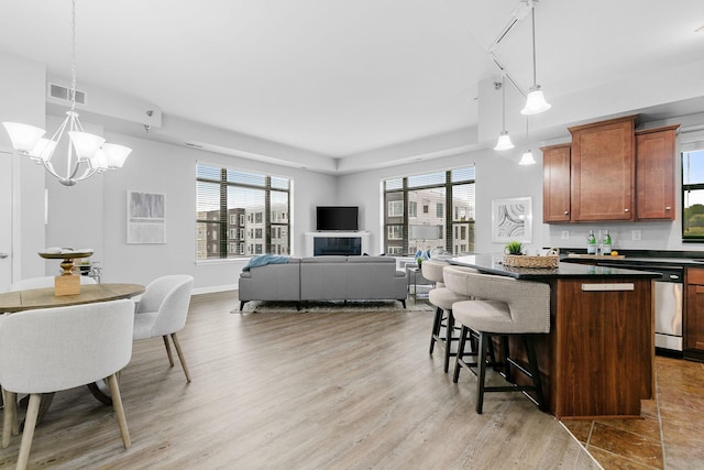 kitchen with a wealth of natural light, a kitchen bar, hanging light fixtures, a center island, and stainless steel dishwasher