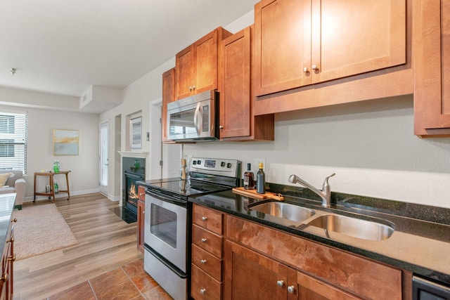 kitchen featuring dark stone countertops, sink, light wood-type flooring, and appliances with stainless steel finishes