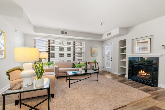 living room with a tiled fireplace, hardwood / wood-style floors, and built in shelves