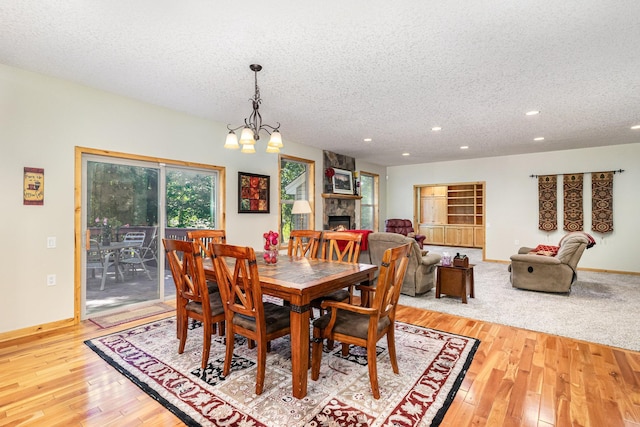 dining space featuring a notable chandelier, a fireplace, light hardwood / wood-style floors, and a textured ceiling