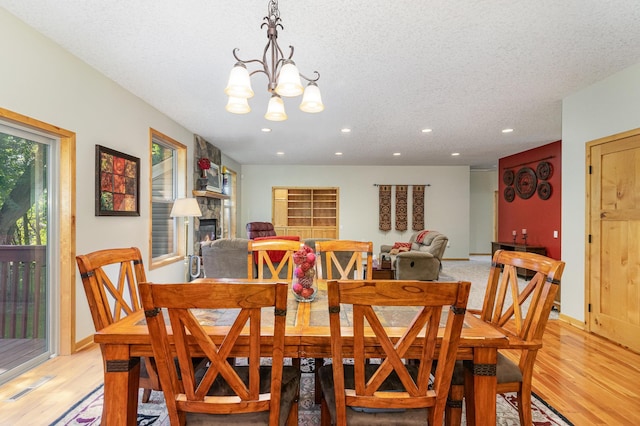 dining area featuring a chandelier, a textured ceiling, a fireplace, and light hardwood / wood-style floors