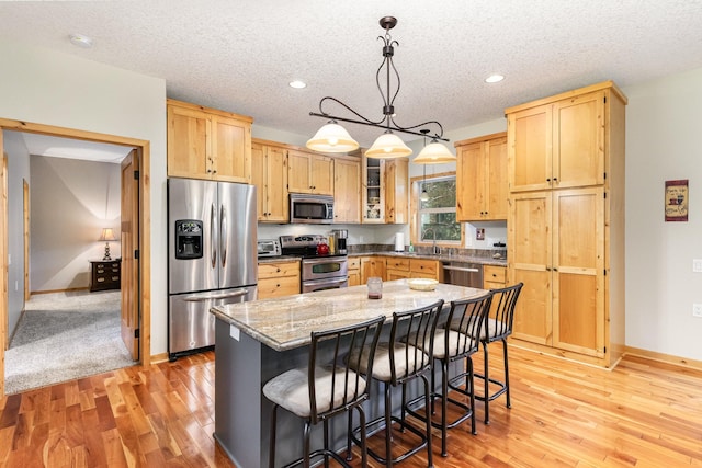 kitchen with a kitchen island, pendant lighting, a kitchen breakfast bar, stainless steel appliances, and light stone countertops