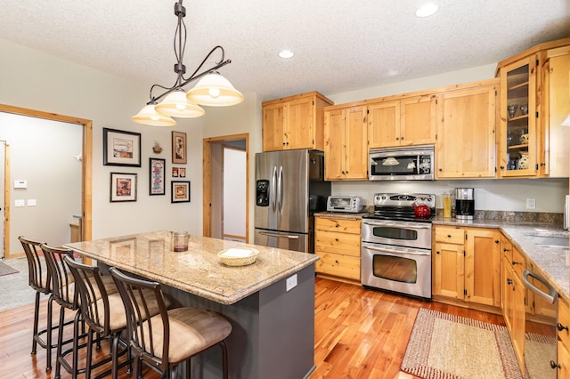 kitchen featuring stainless steel appliances, light stone countertops, a center island, and decorative light fixtures