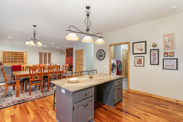 kitchen with washer and dryer, a center island, hanging light fixtures, and light hardwood / wood-style flooring