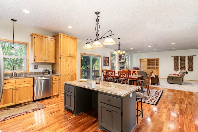 kitchen with sink, light stone countertops, a kitchen island, decorative light fixtures, and stainless steel dishwasher