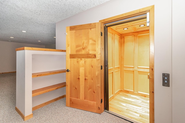 hall featuring elevator, light colored carpet, and a textured ceiling