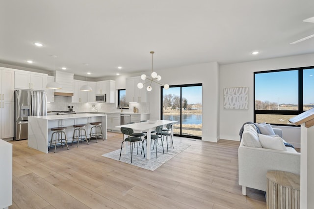 dining space with a water view, light wood-type flooring, sink, and a chandelier