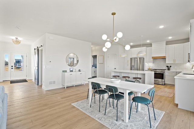 dining space with a barn door, light wood-type flooring, sink, and a chandelier