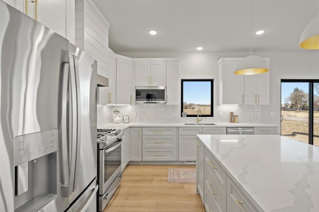 kitchen featuring white cabinetry, sink, stainless steel appliances, light stone counters, and decorative light fixtures