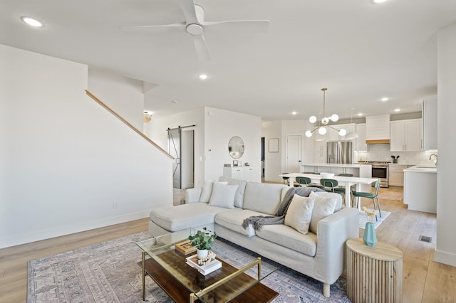 living room with light wood-type flooring, a barn door, ceiling fan with notable chandelier, and sink