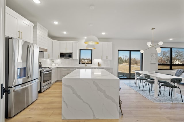 kitchen with white cabinetry, stainless steel appliances, decorative light fixtures, a kitchen island, and light wood-type flooring