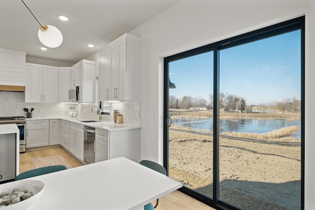 kitchen featuring white cabinets, a water view, sink, hanging light fixtures, and appliances with stainless steel finishes