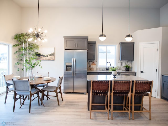 kitchen with stainless steel fridge, backsplash, a healthy amount of sunlight, pendant lighting, and a notable chandelier