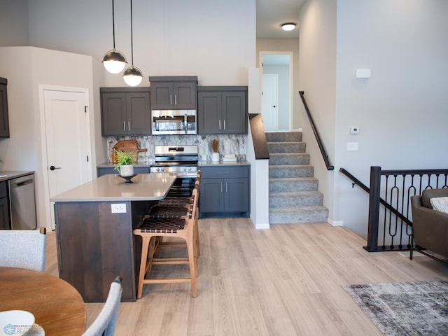 kitchen featuring a center island, backsplash, light hardwood / wood-style flooring, decorative light fixtures, and stainless steel appliances