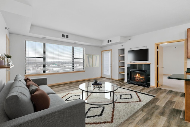 living room featuring hardwood / wood-style flooring, a tiled fireplace, and built in shelves