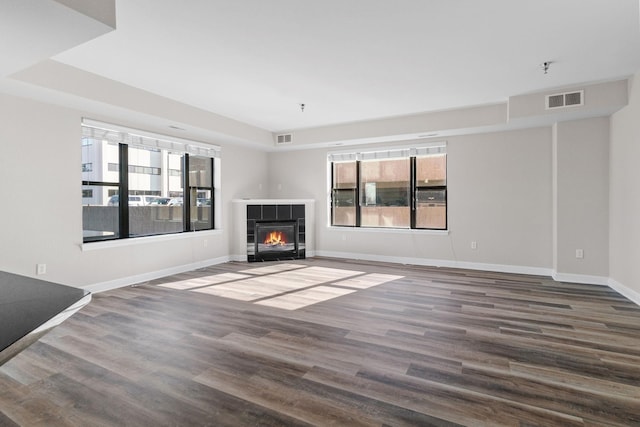 unfurnished living room featuring dark wood-type flooring, a tray ceiling, and a tile fireplace