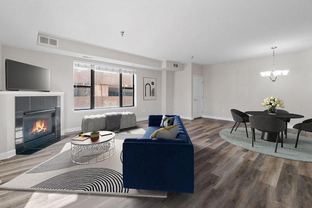 living room with wood-type flooring, a tiled fireplace, and a notable chandelier