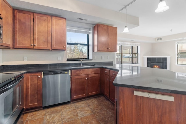 kitchen with a tile fireplace, a wealth of natural light, sink, hanging light fixtures, and stainless steel appliances