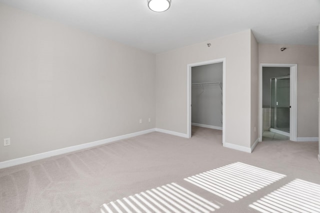 unfurnished bedroom featuring ensuite bathroom, a spacious closet, light carpet, and a closet