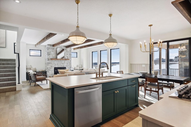 kitchen with sink, a stone fireplace, beamed ceiling, stainless steel dishwasher, and a kitchen island with sink