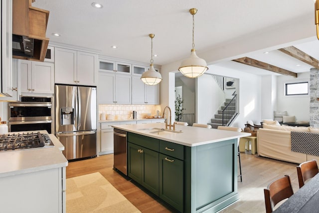 kitchen with appliances with stainless steel finishes, a kitchen island with sink, sink, beam ceiling, and white cabinets