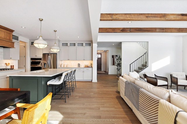 kitchen featuring a center island with sink, white cabinets, decorative light fixtures, beam ceiling, and stainless steel appliances