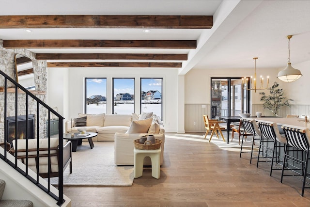 living room with a stone fireplace, beamed ceiling, a notable chandelier, and hardwood / wood-style flooring