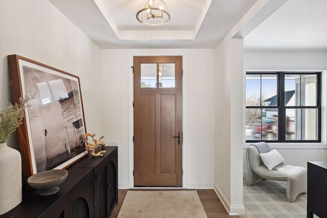 entryway with an inviting chandelier, a raised ceiling, and dark hardwood / wood-style floors