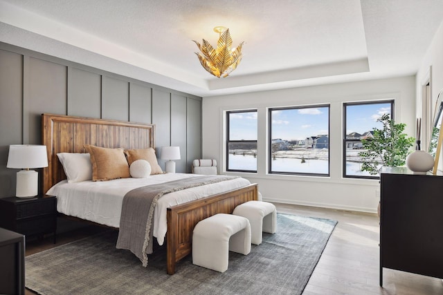 bedroom featuring a tray ceiling, multiple windows, and light hardwood / wood-style floors