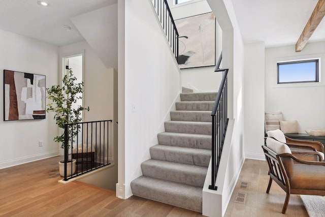 stairway with beamed ceiling and hardwood / wood-style floors