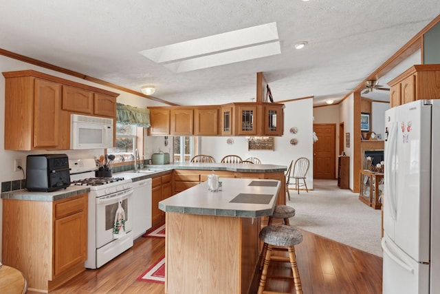 kitchen featuring sink, white appliances, a kitchen breakfast bar, a center island, and vaulted ceiling with skylight