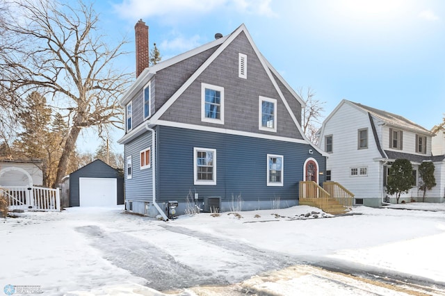 snow covered back of property featuring cooling unit, a garage, and an outdoor structure