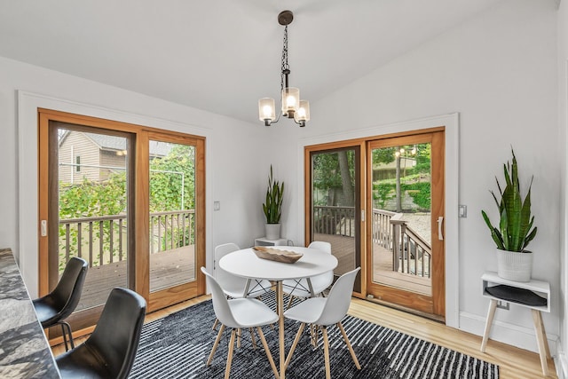 dining room with lofted ceiling, hardwood / wood-style flooring, a healthy amount of sunlight, and a notable chandelier