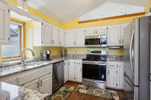 kitchen with vaulted ceiling, appliances with stainless steel finishes, light stone counters, sink, and white cabinetry