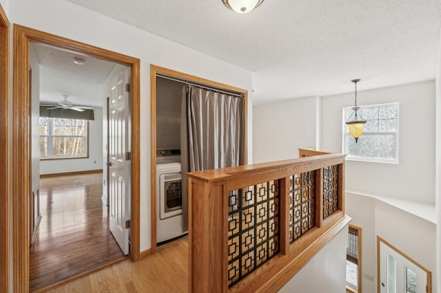 hall featuring washer / clothes dryer, a textured ceiling, and light wood-type flooring