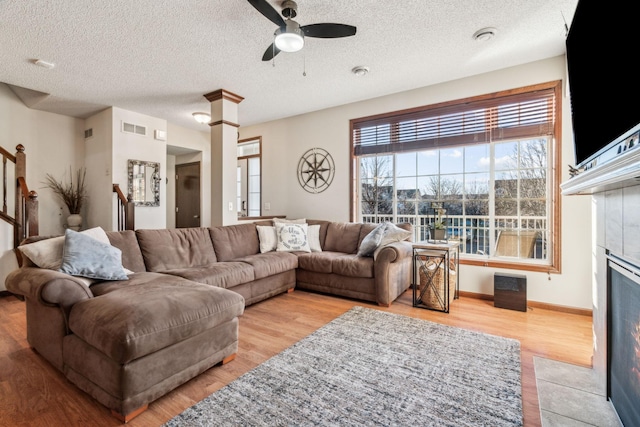 living room with a tiled fireplace, ceiling fan, a textured ceiling, and light wood-type flooring