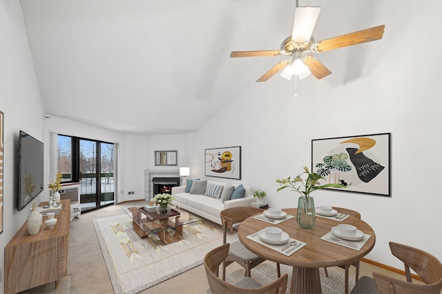 living room featuring light carpet, high vaulted ceiling, baseboards, ceiling fan, and a tile fireplace