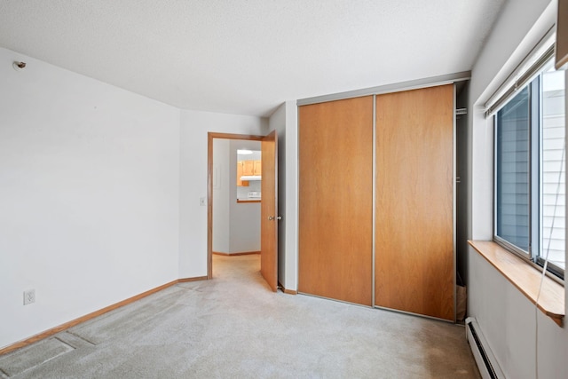 unfurnished bedroom with baseboard heating, a closet, and light colored carpet