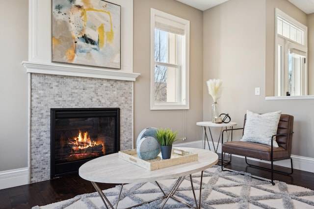 living area with a tile fireplace, baseboards, and wood finished floors