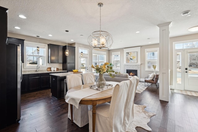 dining space featuring a textured ceiling, recessed lighting, dark wood-style flooring, a glass covered fireplace, and ornate columns