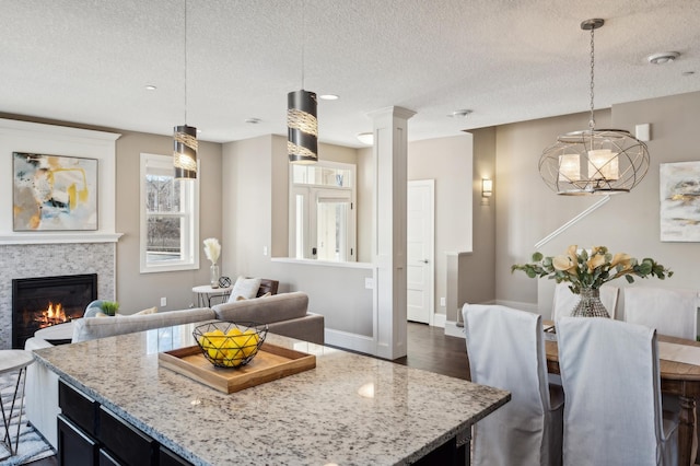 kitchen with a glass covered fireplace, light stone counters, a center island, a textured ceiling, and pendant lighting