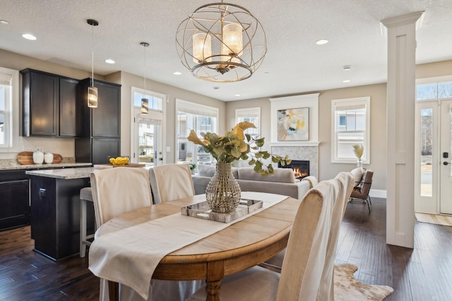 dining space featuring a textured ceiling, recessed lighting, dark wood-style flooring, a lit fireplace, and decorative columns