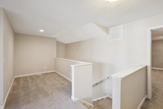 hallway featuring a textured ceiling, an upstairs landing, visible vents, baseboards, and carpet