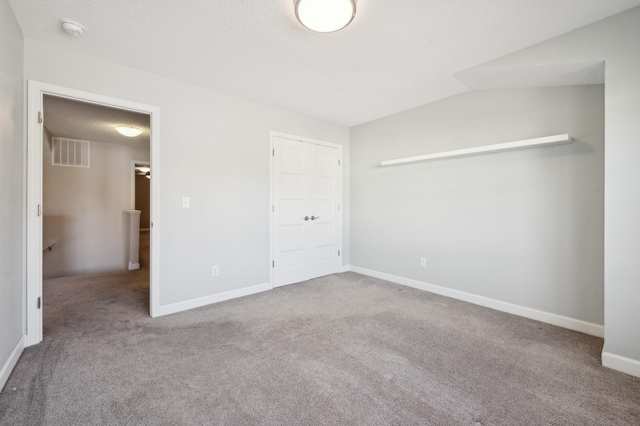 unfurnished bedroom with lofted ceiling, a textured ceiling, carpet floors, visible vents, and baseboards