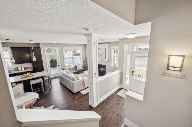 entryway with a warm lit fireplace, ornate columns, dark wood-style floors, and baseboards