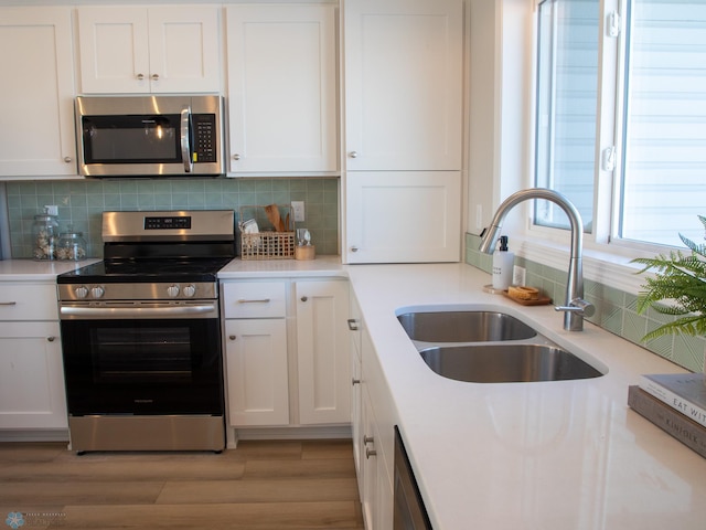 kitchen with light wood-type flooring, backsplash, white cabinetry, appliances with stainless steel finishes, and sink