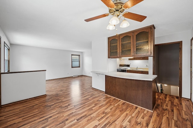 kitchen with ceiling fan, backsplash, range with gas stovetop, dark hardwood / wood-style flooring, and kitchen peninsula