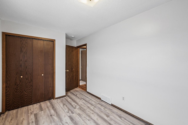 unfurnished bedroom with a textured ceiling, light wood-type flooring, and a closet