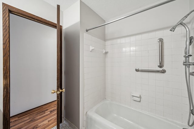 bathroom featuring tiled shower / bath combo, wood-type flooring, and a textured ceiling