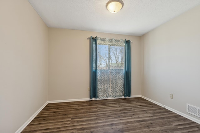 empty room featuring dark wood-type flooring, baseboards, visible vents, and a textured ceiling